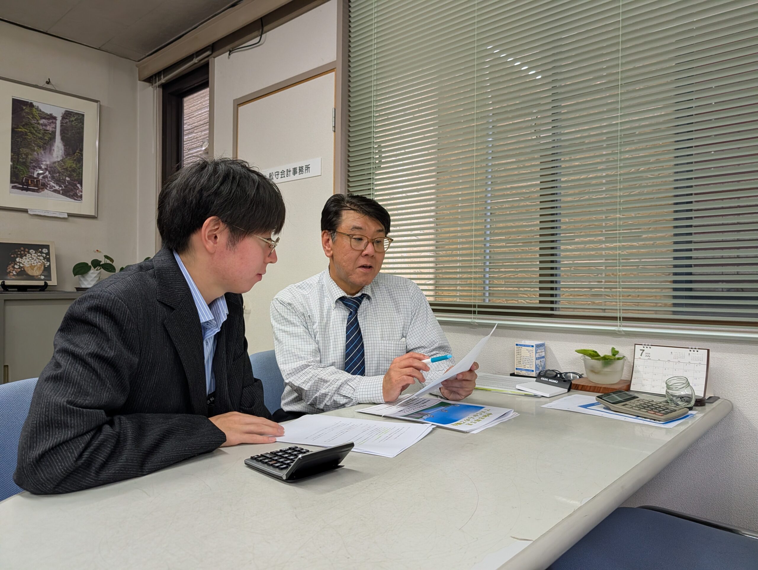 先輩スタッフに資料を確認しながら相談する若手スタッフ